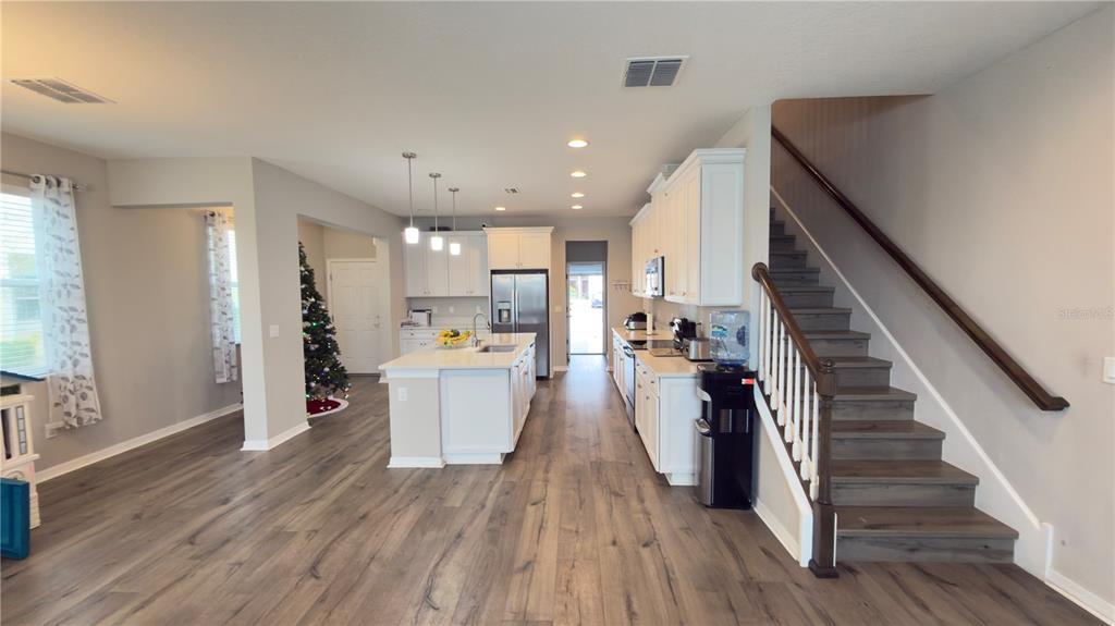 An open-concept kitchen features white cabinetry, a center island, and wood-look flooring near a staircase — 2501 STAPLEFORD PLACE, WESLEY CHAPEL, FL