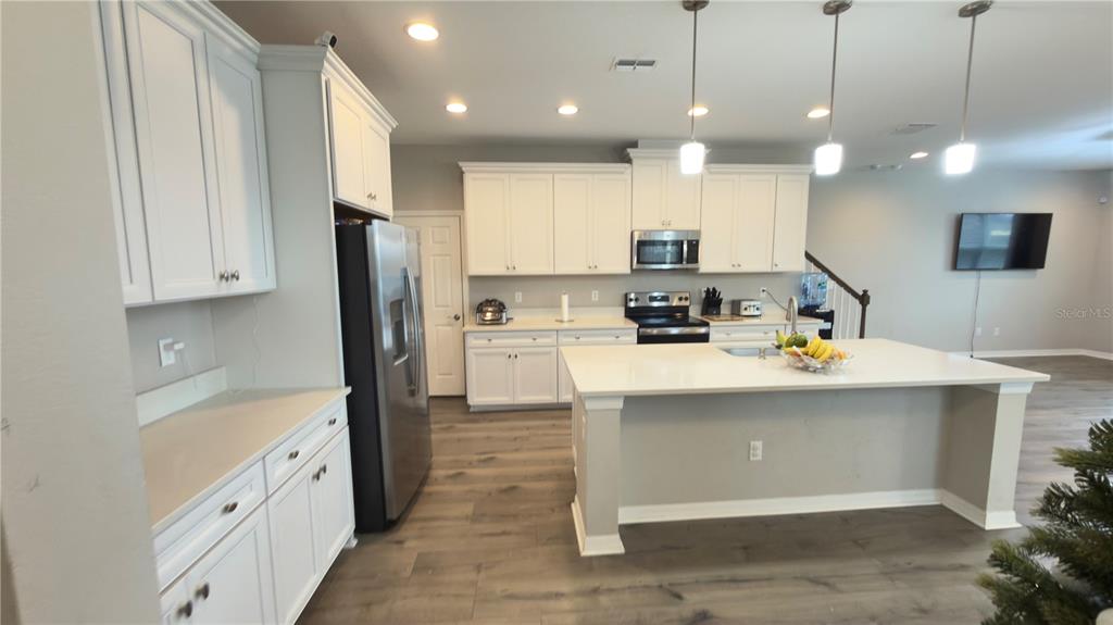 A kitchen features white cabinets, stainless steel appliances, a large island, and light wood flooring — 2501 STAPLEFORD PLACE, WESLEY CHAPEL, FL