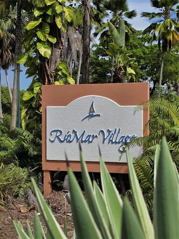 A sign for Rio Mar Village stands outdoors surrounded by lush tropical plants and palm trees — 802 RIO MAR VILLAGE, RIO GRANDE, PR