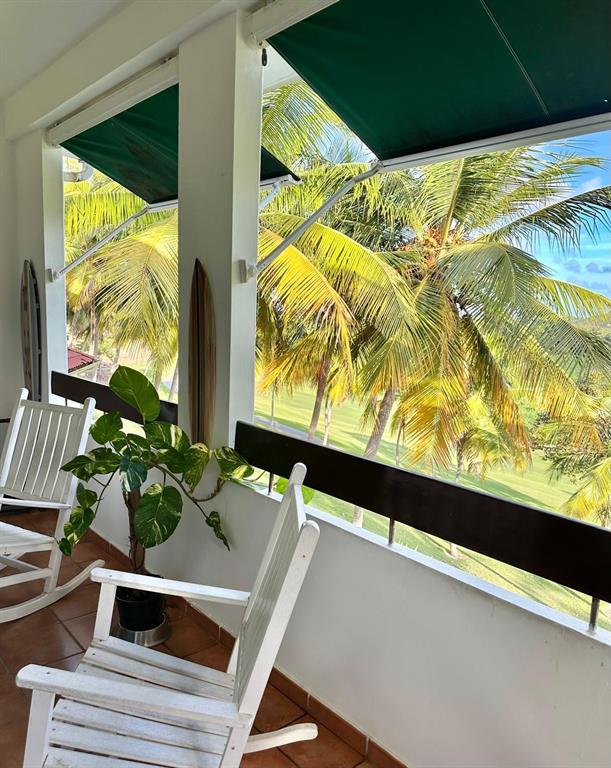 A balcony features two white rocking chairs, a potted plant, and views of palm trees — 802 RIO MAR VILLAGE, RIO GRANDE, PR