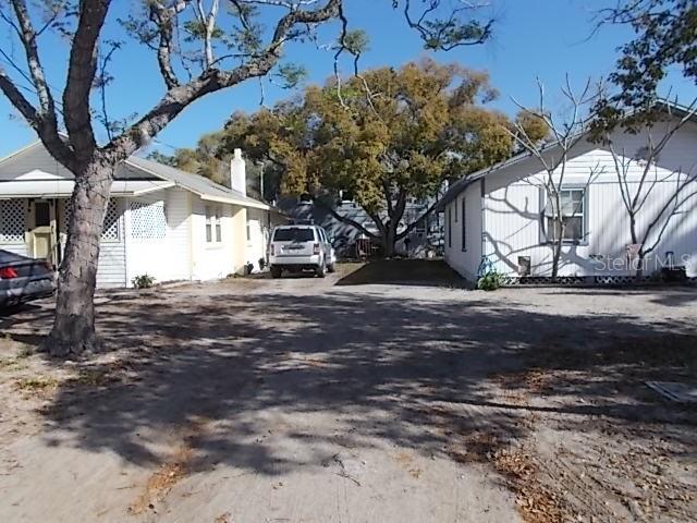 A gravel driveway sits between two white single-story houses with a large tree in back — 518 6TH AVENUE SW, LARGO, FL