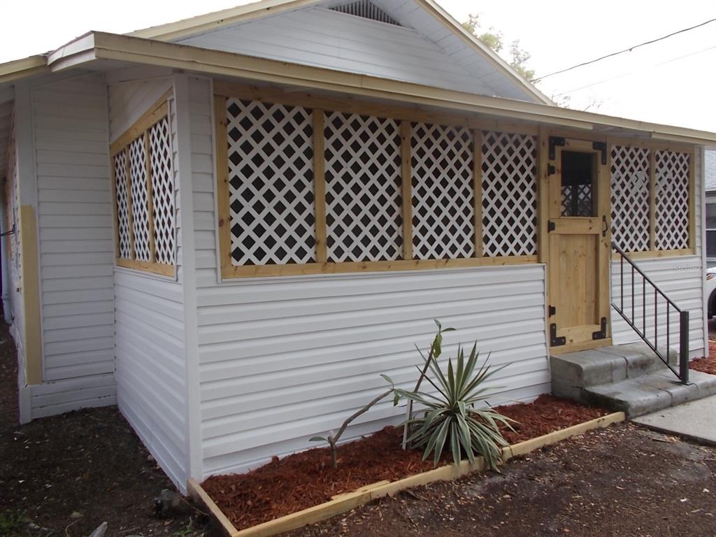 A white house features a screened-in porch with wood framing, lattice panels, and a wooden door — 518 6TH AVENUE SW, LARGO, FL