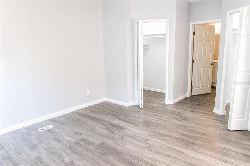 An empty room features light gray walls, wood-look flooring, a walk-in closet, and two doors — 4517 LA FORCE STREET, ZEPHYRHILLS, FL