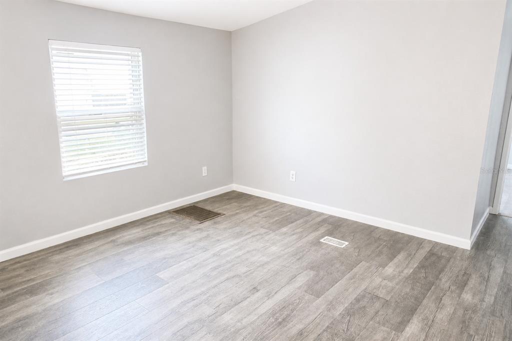An empty room features gray walls, wood-look flooring, a window with blinds, and floor vents — 4517 LA FORCE STREET, ZEPHYRHILLS, FL