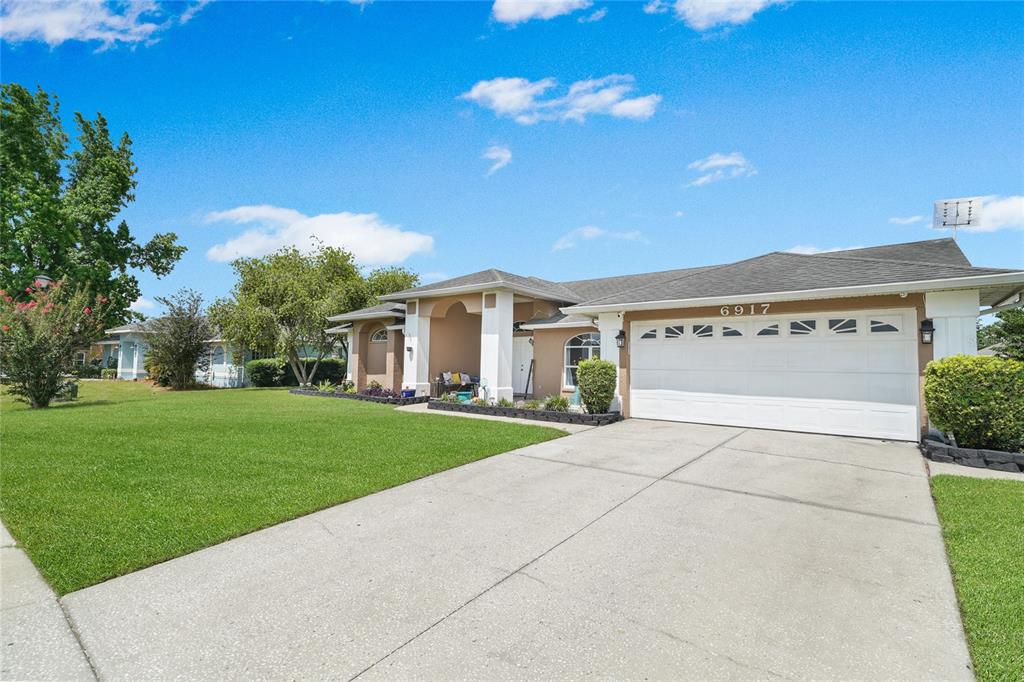 A single-story house with a tan exterior, a two-car garage, and a large front lawn — 6917 ASHBURY DRIVE, LAKELAND, FL