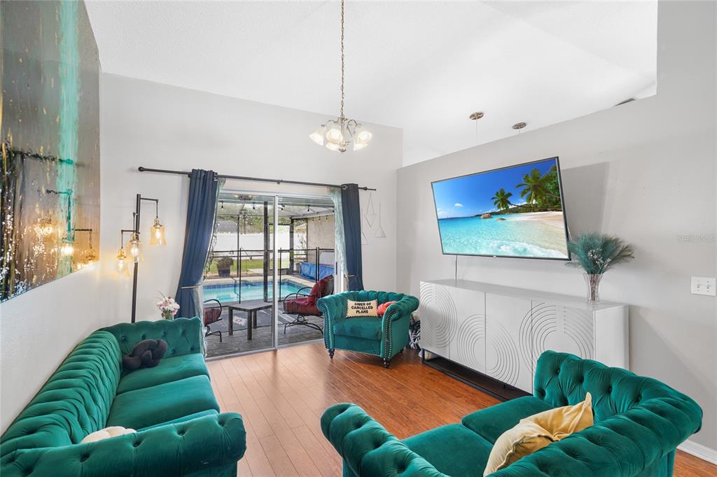 A living room features two emerald green tufted sofas, a white media console, and pool views — 6917 ASHBURY DRIVE, LAKELAND, FL