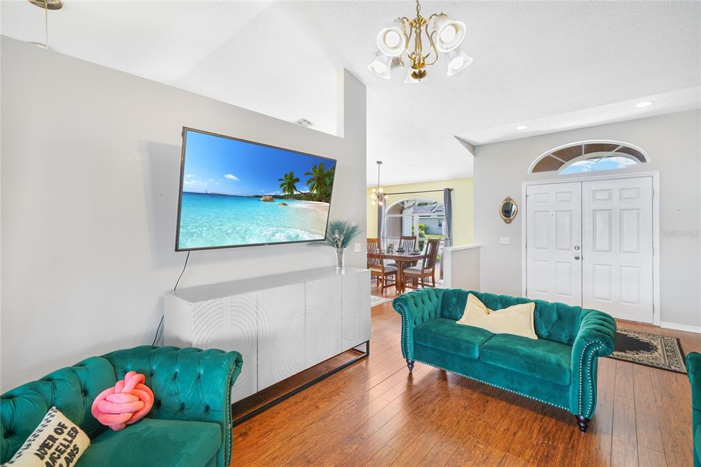 A living room features green tufted sofas, a white media console, and a wall-mounted television — 6917 ASHBURY DRIVE, LAKELAND, FL