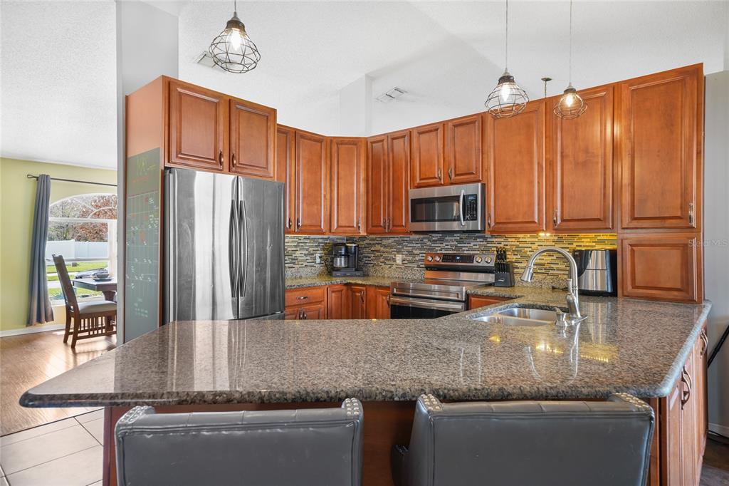 A kitchen features wood cabinets, granite countertops, stainless steel appliances, and a breakfast bar — 6917 ASHBURY DRIVE, LAKELAND, FL