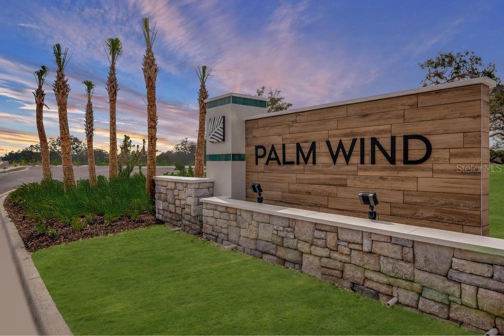 A stone and wood-paneled monument sign for Palm Wind stands beside palm trees outdoors — 13747 SQUALL LANE, HUDSON, FL