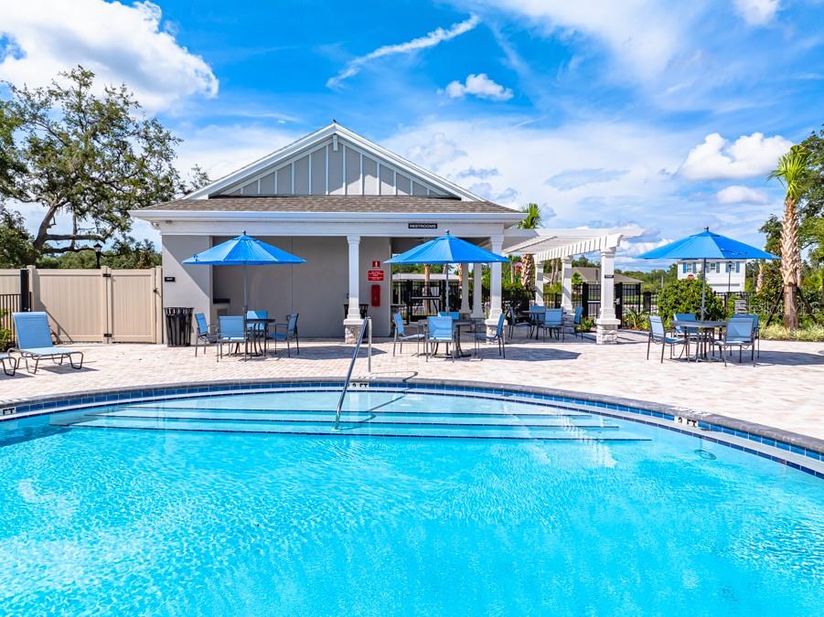 A swimming pool sits in front of a community building with outdoor seating and umbrellas — 13747 SQUALL LANE, HUDSON, FL