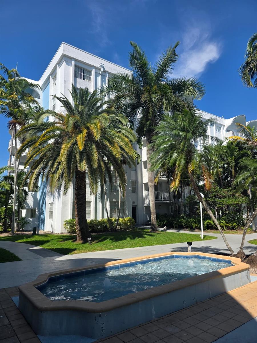 A multi-story white apartment building stands behind a small rectangular fountain and palm trees — 486 NW 165th St Rd # 405, Miami FL 33169, MIAMI, FL