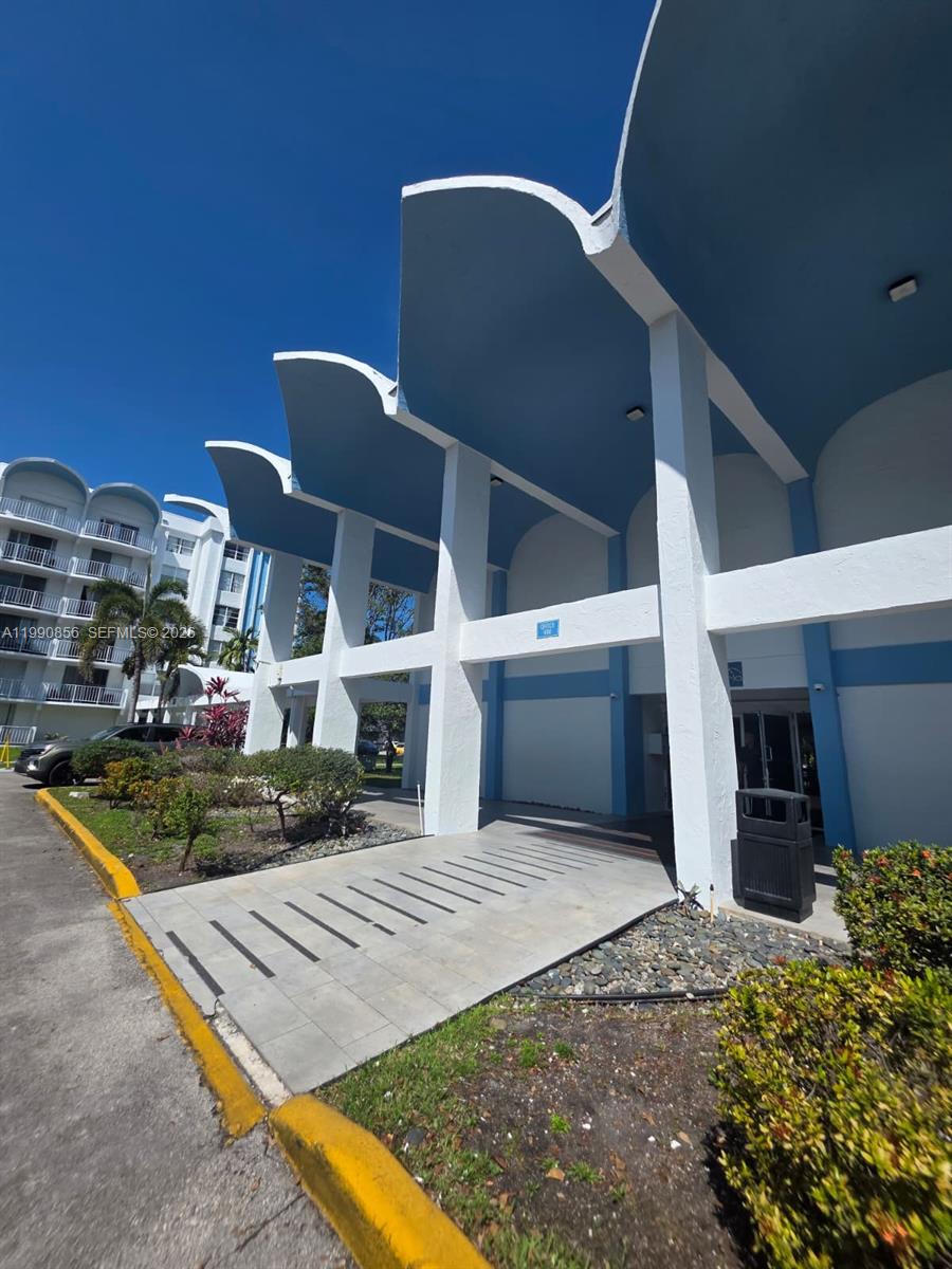 The exterior of a building features a white concrete structure with blue curved roof accents — 486 NW 165th St Rd # 405, Miami FL 33169, MIAMI, FL