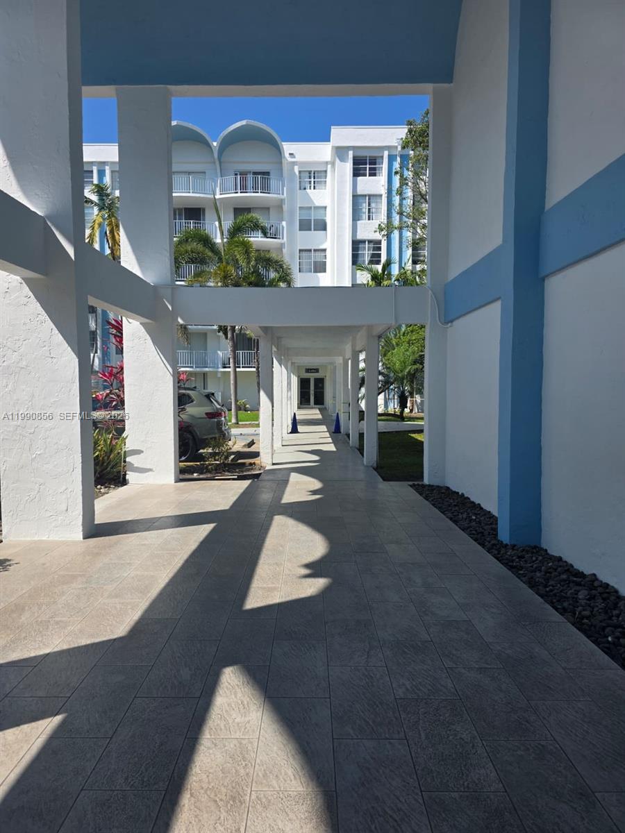 A covered walkway with tiled flooring leads toward a multi-story apartment building — 486 NW 165th St Rd # 405, Miami FL 33169, MIAMI, FL