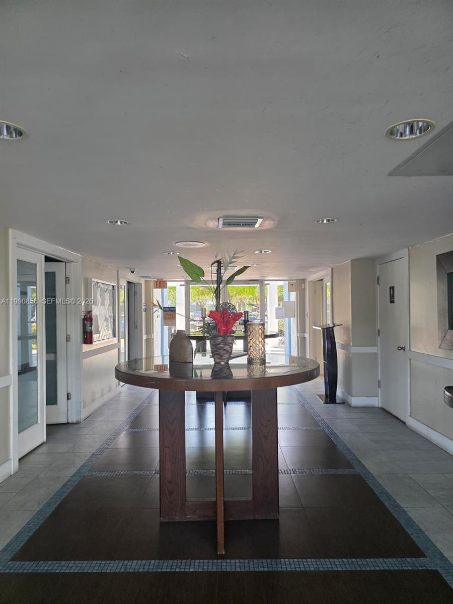 A round wooden table with a floral centerpiece sits in a tiled building lobby — 486 NW 165th St Rd # 405, Miami FL 33169, MIAMI, FL
