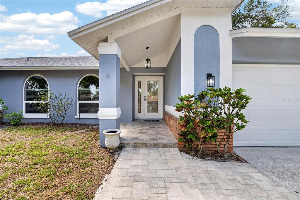 The exterior of a house features a blue facade, arched windows, and a paved walkway — 1668 ALLENS RIDGE DRIVE N, PALM HARBOR, FL