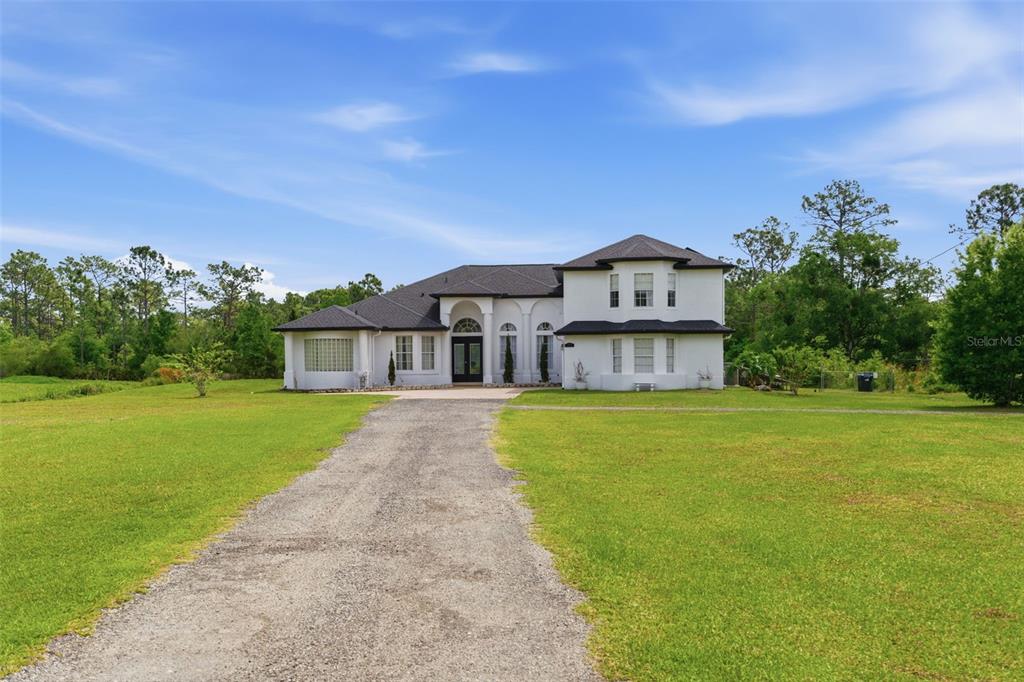 A two-story white house with a gravel driveway sits on a large grassy lot — 4529 CAESAR AVENUE, ORLANDO, FL
