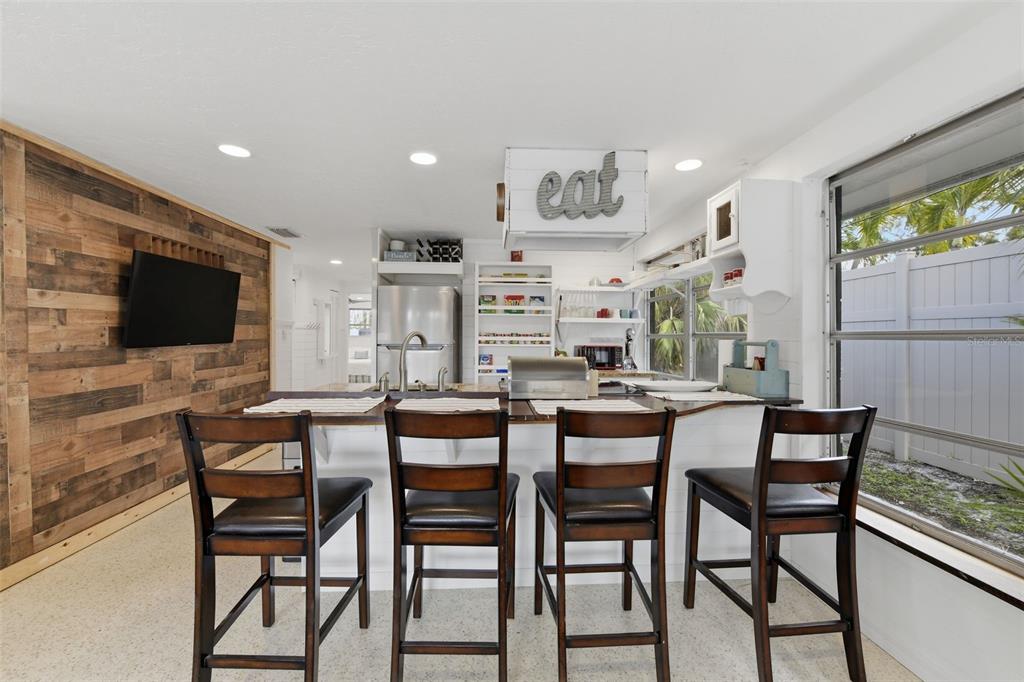 A kitchen features a wooden accent wall, a breakfast bar with four chairs, and cabinetry — 8456 MIDNIGHT PASS ROAD, SARASOTA, FL