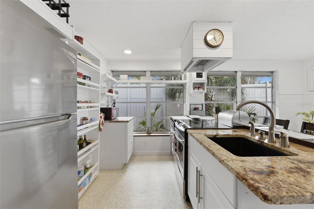 A kitchen features white cabinetry, a granite countertop, a stainless steel refrigerator, and open shelving — 8456 MIDNIGHT PASS ROAD, SARASOTA, FL