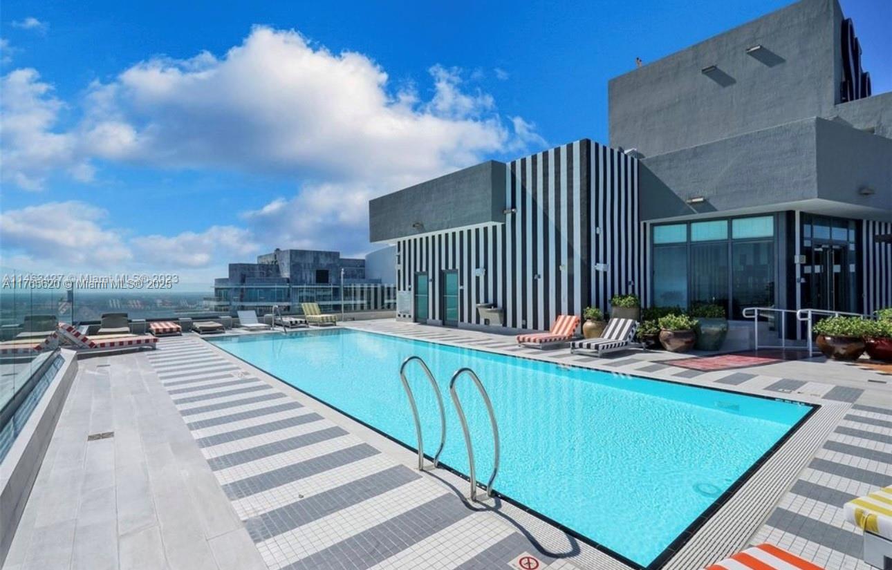 A rooftop swimming pool with lounge chairs on a tiled deck beside a modern building — 1300 S Miami Ave # 3108, Miami FL 33130, MIAMI, FL