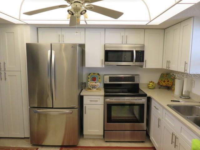 A kitchen features white cabinets, stainless steel appliances, and a ceiling fan — 1400 1ST AVENUE W UNIT 504, BRADENTON, FL