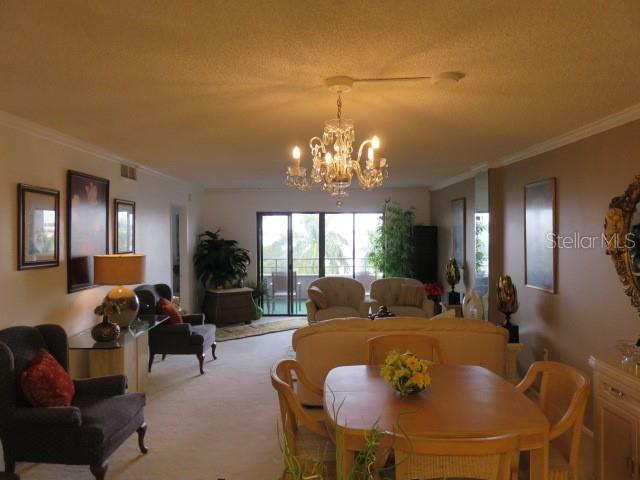 A living and dining area features a crystal chandelier, beige carpeting, and neutral-toned furniture — 1400 1ST AVENUE W UNIT 504, BRADENTON, FL