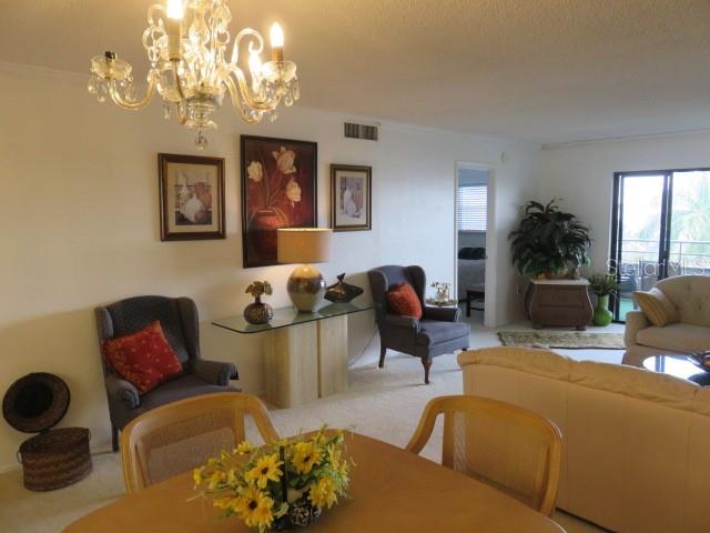A living room features a crystal chandelier, a glass-topped console table, and neutral-toned furniture — 1400 1ST AVENUE W UNIT 504, BRADENTON, FL