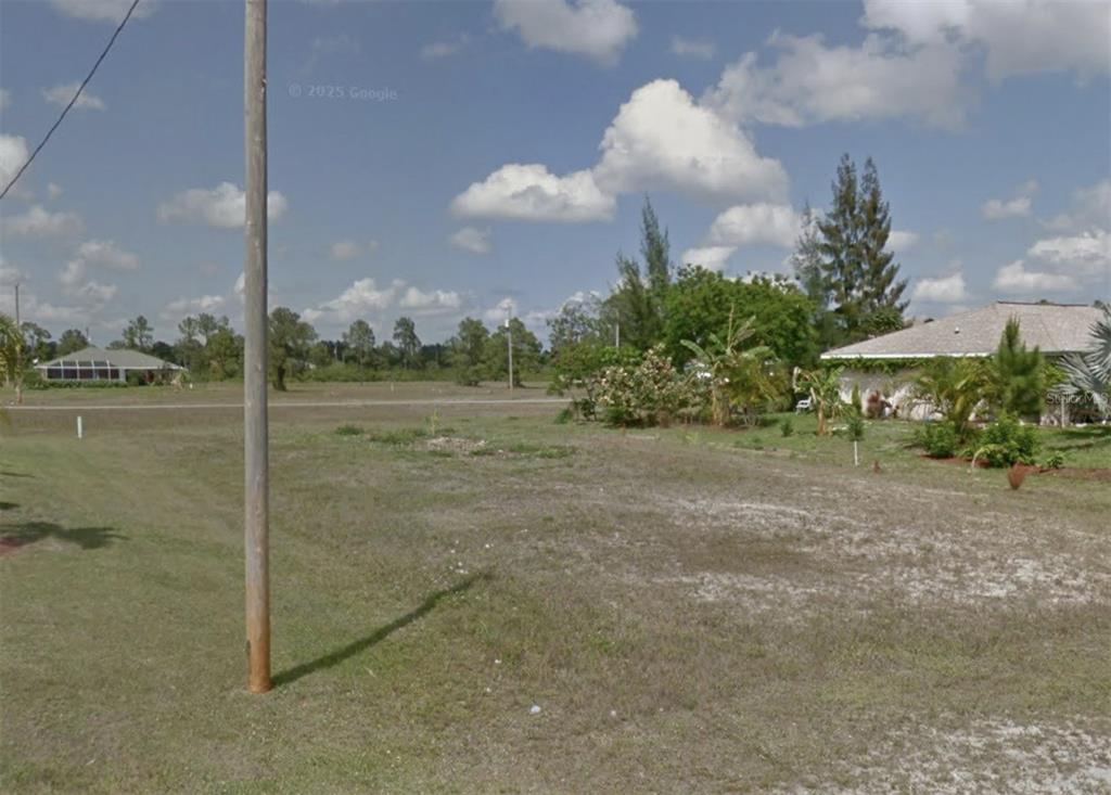 A vacant, grassy lot sits between a utility pole and a neighboring residential house — 2215 NE 34TH LN, CAPE CORAL, FL