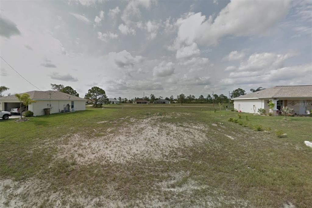 A vacant residential lot sits between two single-story houses under a cloudy sky — 2215 NE 34TH LN, CAPE CORAL, FL