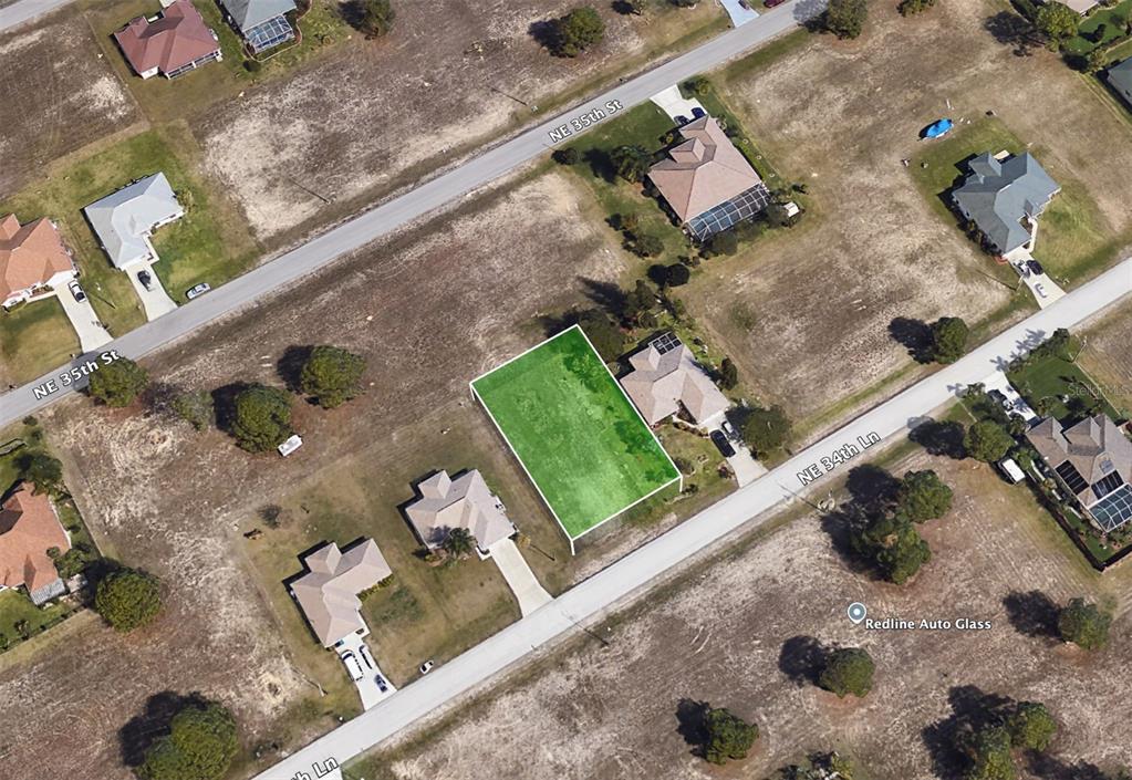 An aerial view shows a vacant, rectangular lot highlighted in green between two residential streets — 2215 NE 34TH LN, CAPE CORAL, FL