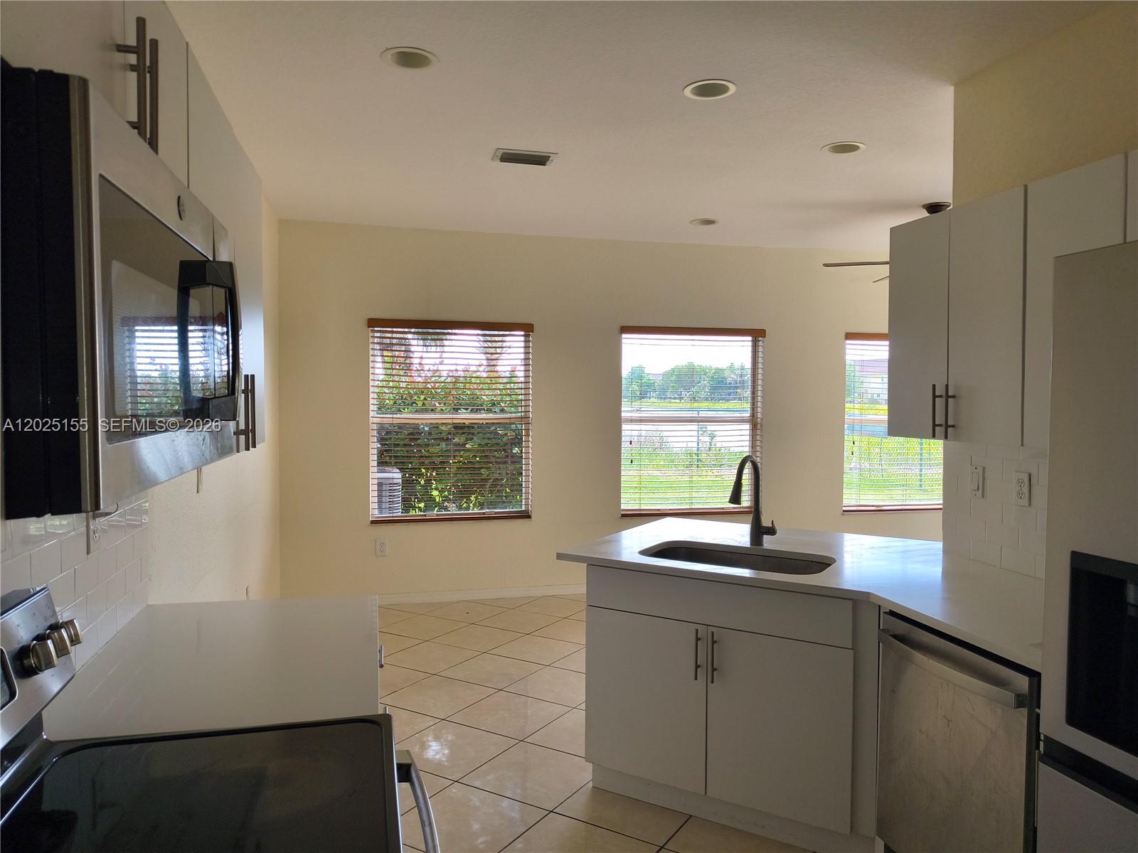 A kitchen features white cabinets, stainless steel appliances, a sink island, and tile flooring — 1645 SE 20th Rd # 1645, Homestead FL 33035, HOMESTEAD, FL