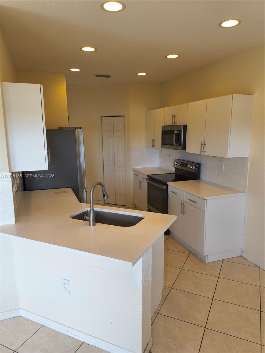 A kitchen features white cabinets, stainless steel appliances, a peninsula sink, and tile flooring — 1645 SE 20th Rd # 1645, Homestead FL 33035, HOMESTEAD, FL