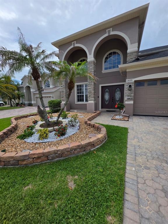 A two-story house features a stone-accented arched entryway, a paved driveway, and a landscaped garden — 12039 BLAIREMONT WAY, ORLANDO, FL
