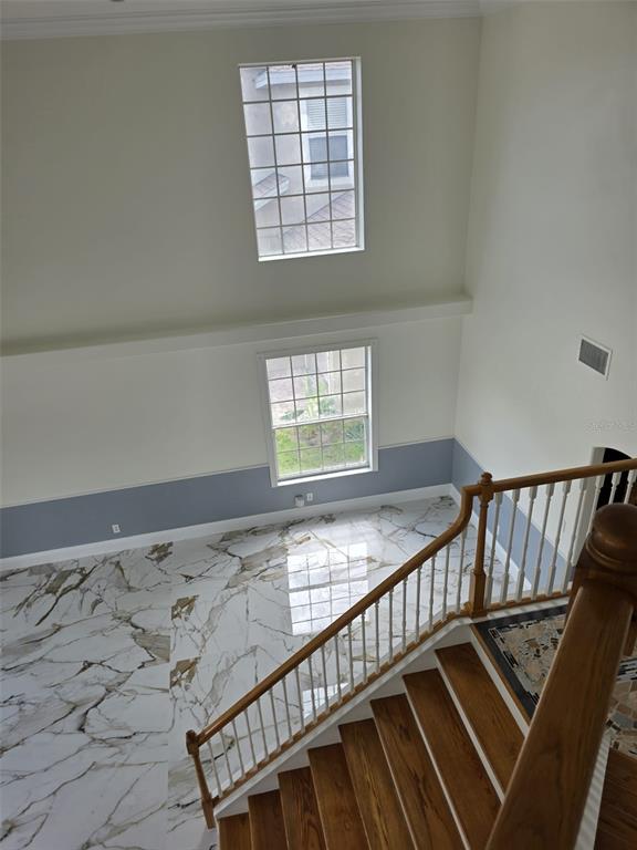A high-angle view shows a two-story room with marble-look tile floors, stacked windows, and a wooden staircase — 12039 BLAIREMONT WAY, ORLANDO, FL
