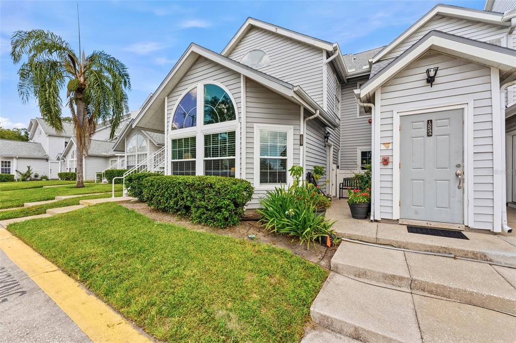 A gray-sided townhouse exterior features a front door, a large arched window, and landscaping — 12237 ARMENIA GABLES CIR, TAMPA, FL