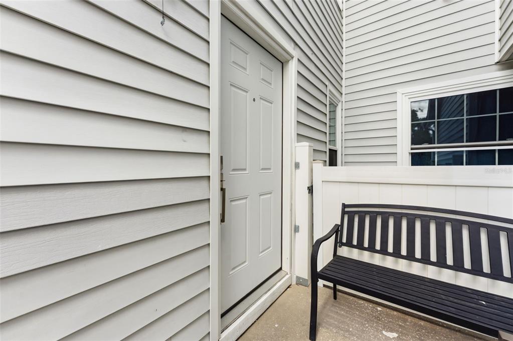 A white front door with a black bench sits on a concrete porch — 12237 ARMENIA GABLES CIR, TAMPA, FL