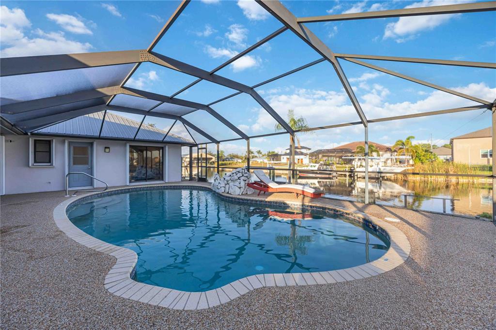 A screened-in pool area features a kidney-shaped pool, a rock waterfall, and waterfront views — 10534 ALPACA CIRCLE, PORT CHARLOTTE, FL