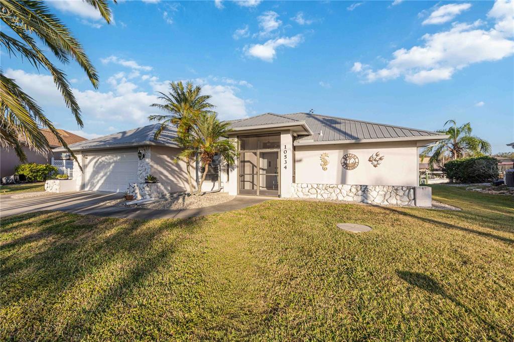 A single-story house with a metal roof, stone accents, and a screened front entryway — 10534 ALPACA CIRCLE, PORT CHARLOTTE, FL