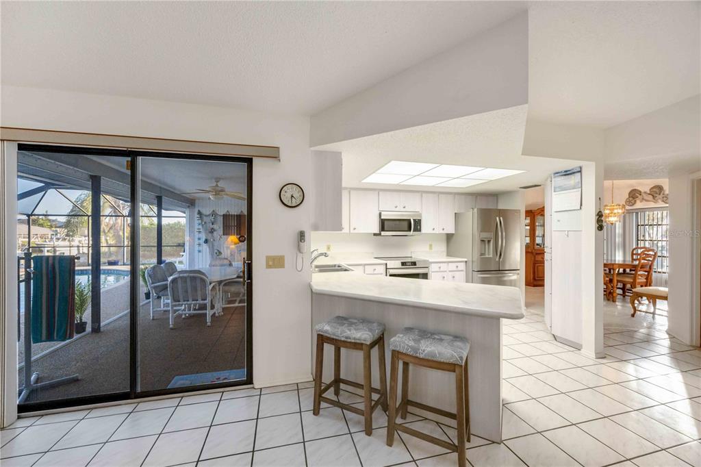 A kitchen with white cabinets and a breakfast bar overlooks a patio and swimming pool — 10534 ALPACA CIRCLE, PORT CHARLOTTE, FL