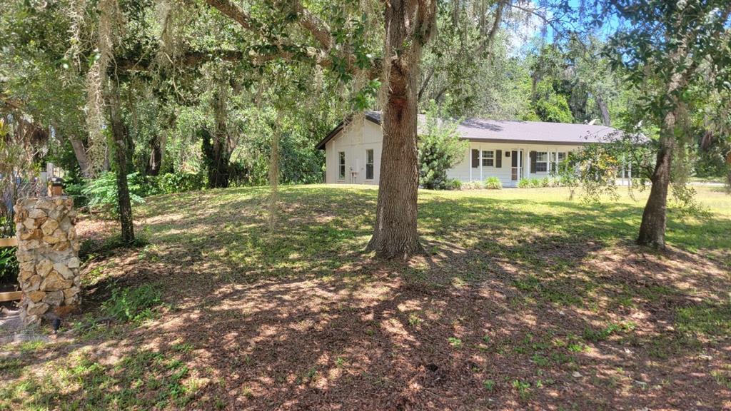 A single-story house with a light-colored exterior sits on a grassy hill among trees — 3036 LOWERY DRIVE, OVIEDO, FL