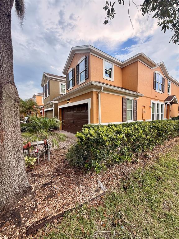 A two-story orange stucco townhouse features a brown garage door and a landscaped front yard — 9412 STRONGBARK LANE, ORLANDO, FL