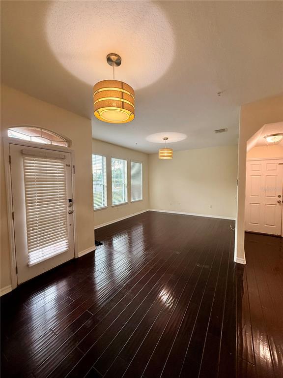 An empty room features dark hardwood floors, two drum pendant lights, and a front door — 9412 STRONGBARK LANE, ORLANDO, FL