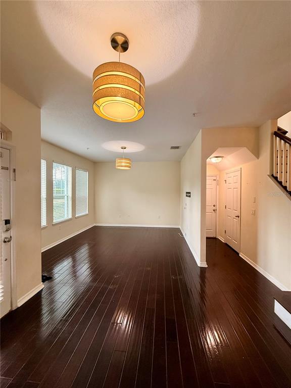 An empty room features dark hardwood floors, two pendant lights, and white walls — 9412 STRONGBARK LANE, ORLANDO, FL