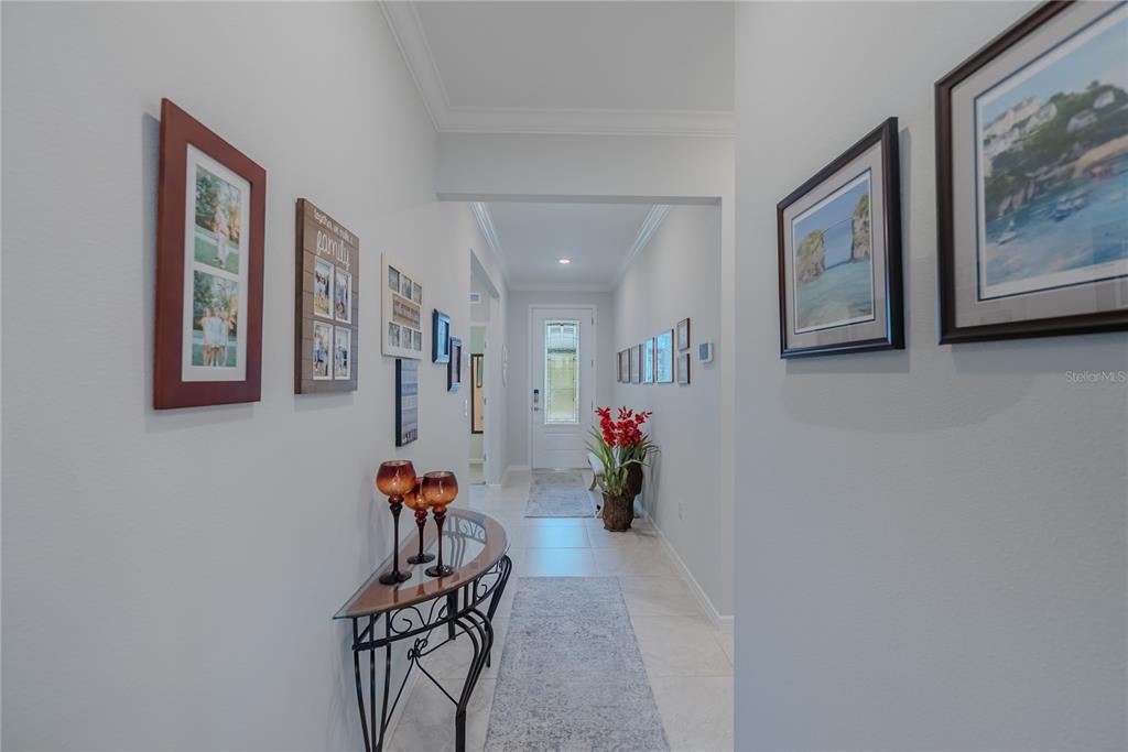 A hallway with light-colored walls, tile flooring, a console table, and several framed wall pictures — 9426 SW 54TH STREET, OCALA, FL