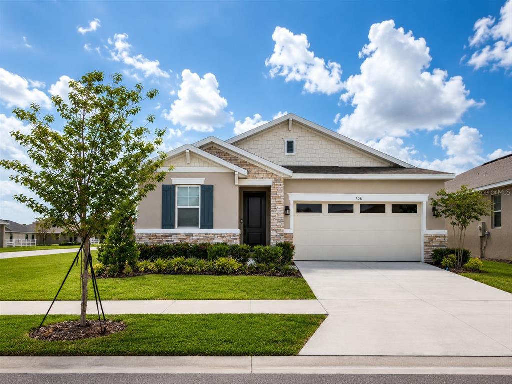 A single-story house with a beige stucco exterior, stone accents, and a two-car garage — 708 GRIFFON AVENUE, LAKE ALFRED, FL