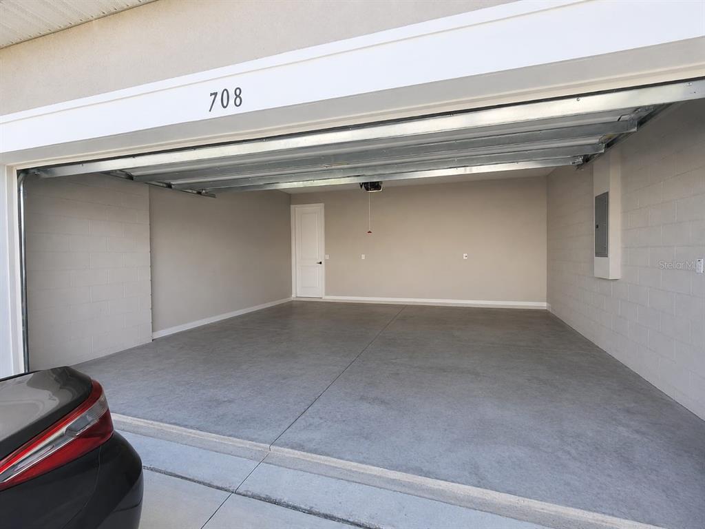 An empty two-car garage features concrete flooring, light gray walls, and a white interior door — 708 GRIFFON AVENUE, LAKE ALFRED, FL