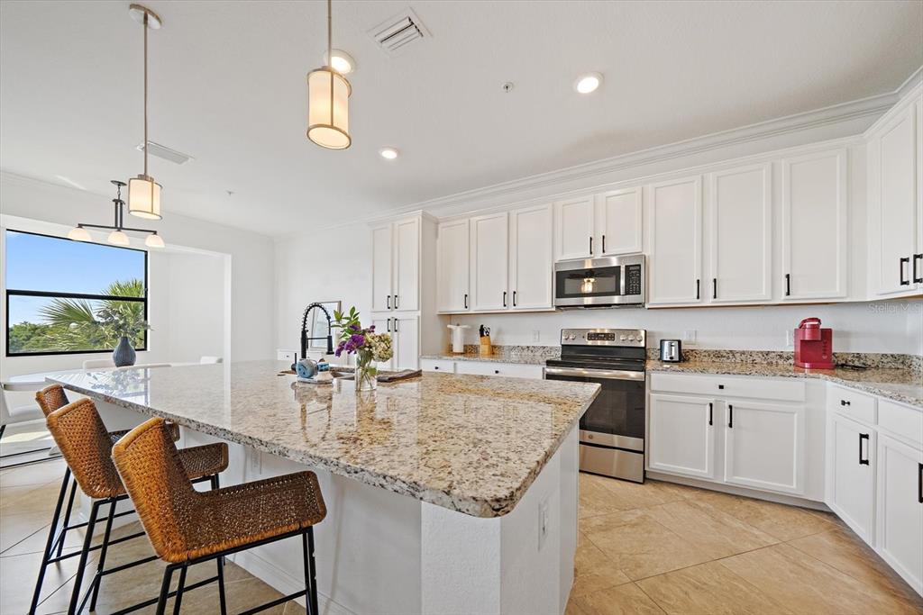 A kitchen features white cabinets, granite countertops, a large island, and two woven bar stools — 17006 VARDON TERRACE UNIT 401, BRADENTON, FL