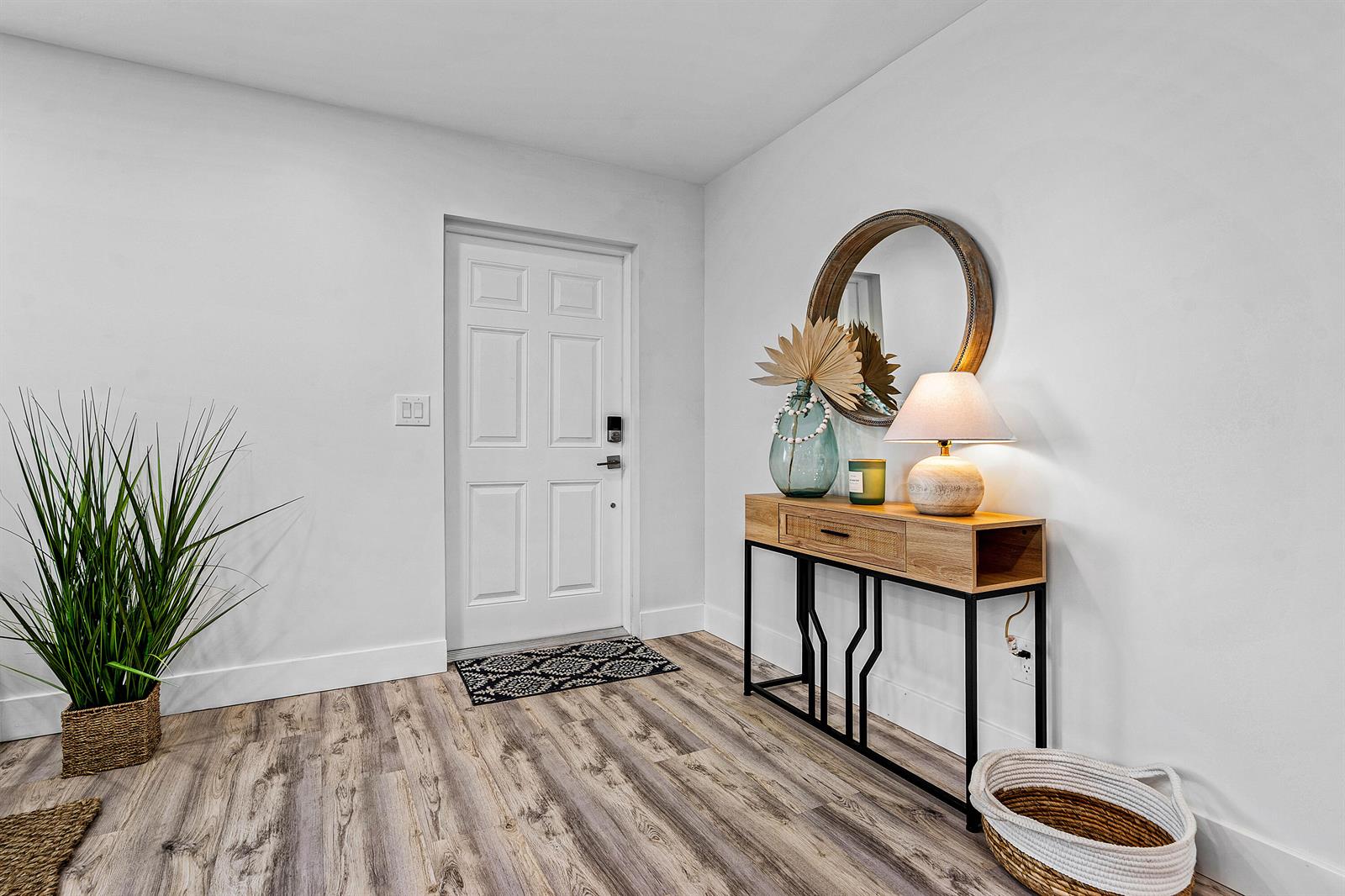 An entryway features a white door, wood-look flooring, a console table, and a round mirror — 2015 SW 18th Drive, Boynton Beach FL 33426, BOYNTON BEACH, FL