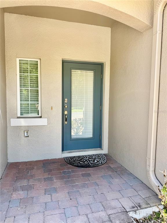 A blue front door with a window sits beside a small window on a paved porch — 683 EVENING SKY DRIVE, OVIEDO, FL