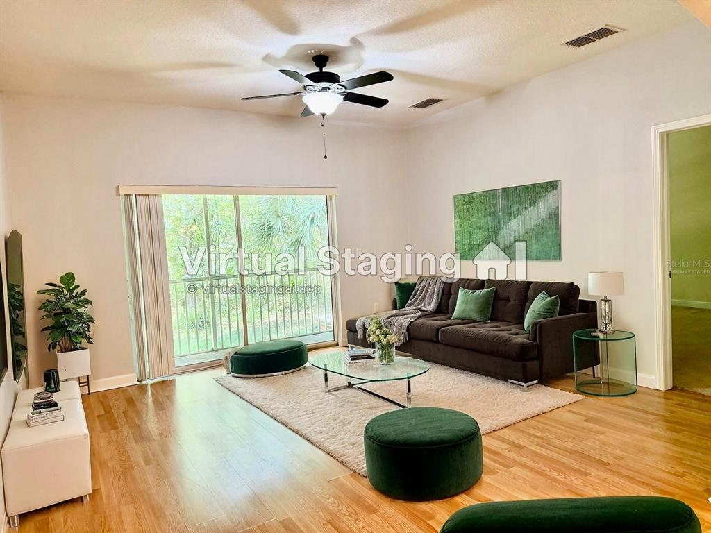 This living room features wood flooring, a dark sofa, a glass coffee table, and a ceiling fan — 683 EVENING SKY DRIVE, OVIEDO, FL