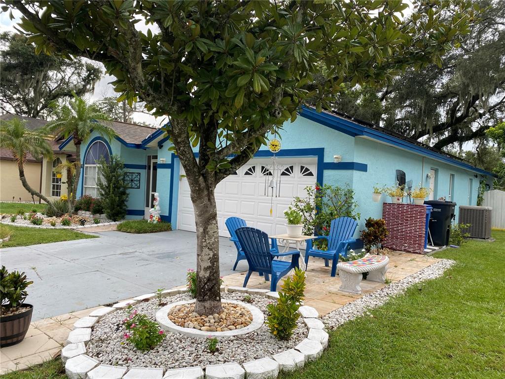 A light blue house features a front yard with a tree, stone landscaping, and blue chairs — 1420 WINDJAMMER PLACE, VALRICO, FL